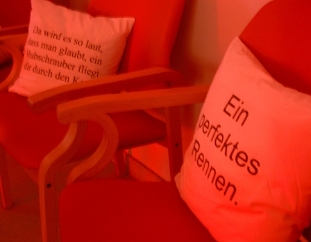 Zwei Pölster auf Sesseln im Altersheim. Einer trägt die Aufschrift: "Da wird es so laut, dass man glaubt, ein Hubschrauber fliegt dir durch den Kopf."